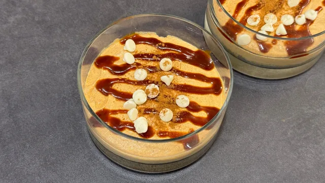 Two pumpkin spice no-bake cheesecakes in glass cups topped with caramel drizzle and white chocolate chips.
