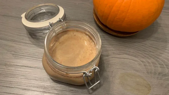 Homemade pumpkin spice sauce stored in a glass mason jar with an airtight lid, displayed next to a fresh pumpkin.