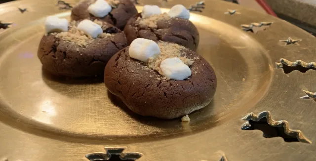 Chocolate s'mores cookies topped with marshmallows on a gold plate with star cutouts.