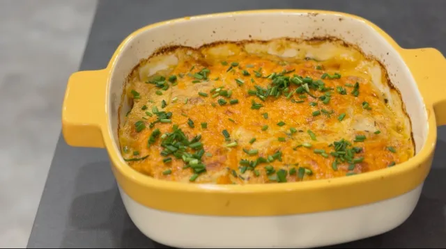 Cheesy scalloped potatoes in a yellow and white baking dish, topped with melted cheddar cheese and fresh chives.