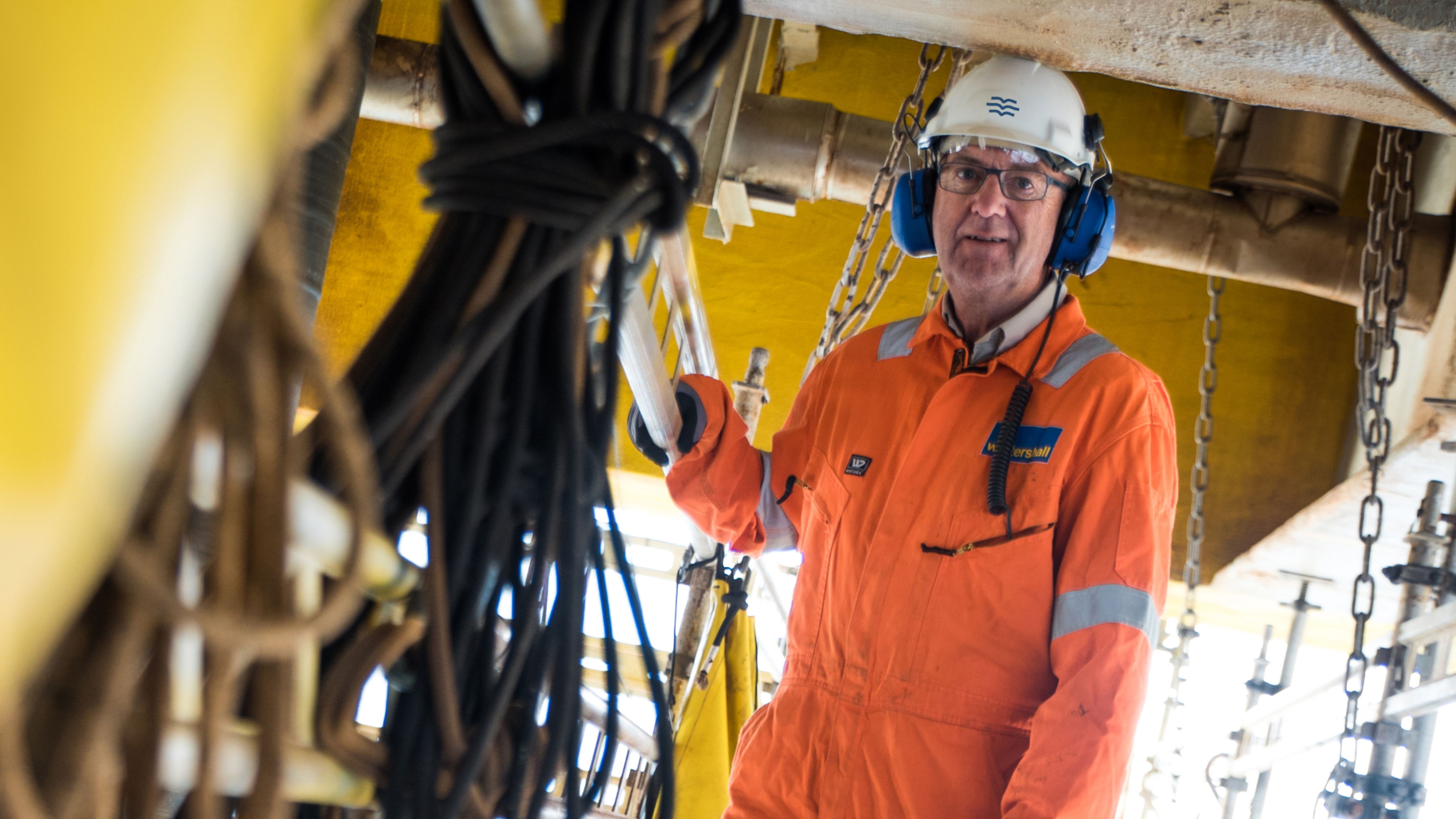 Worker in an orange overall and white helmet with Sjømannskirken blue symbol