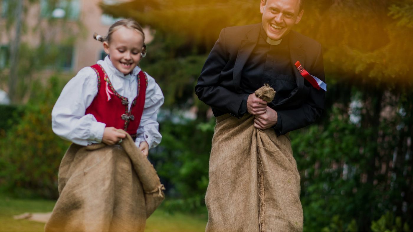 Sjømannskirken logo med to barn som hopper i potetsekk i en grønn hage i bakgrunnen