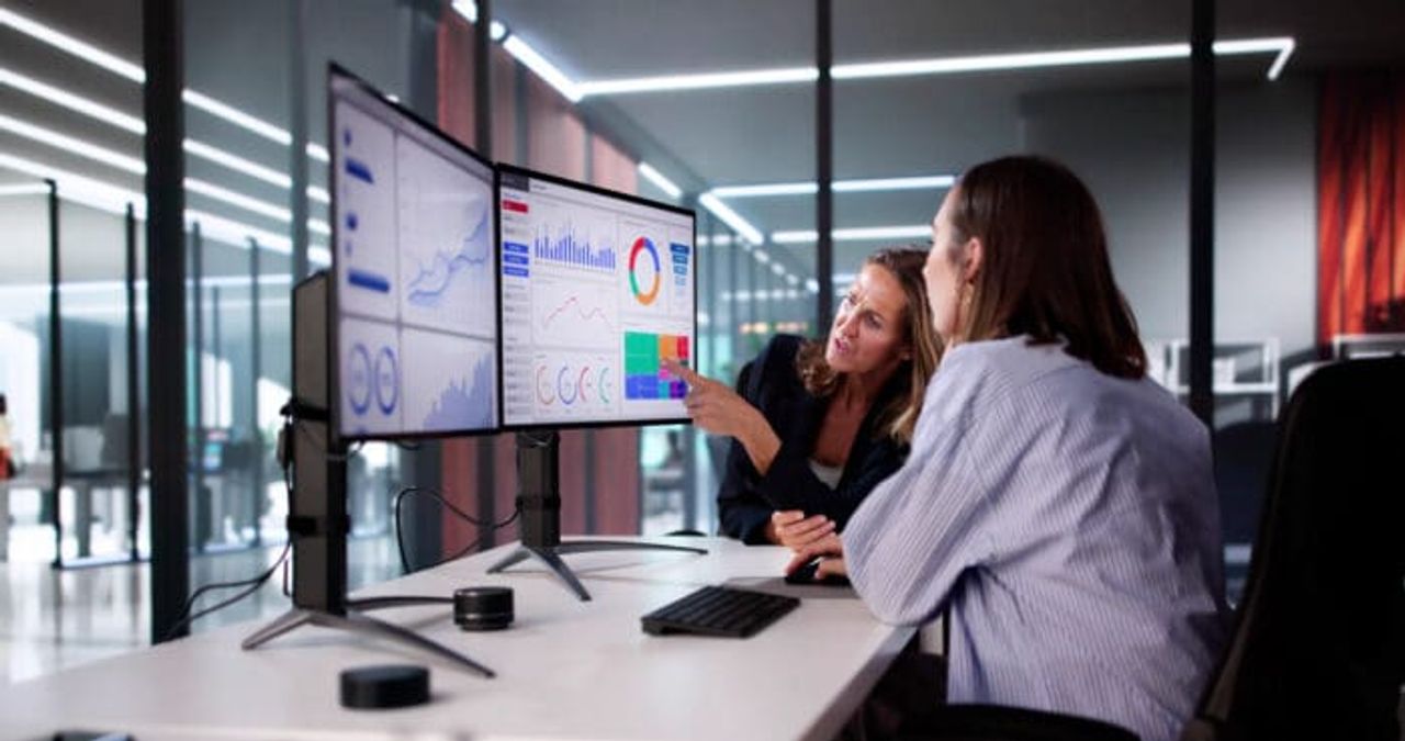 Two colleagues analyzing data on dual monitors.
