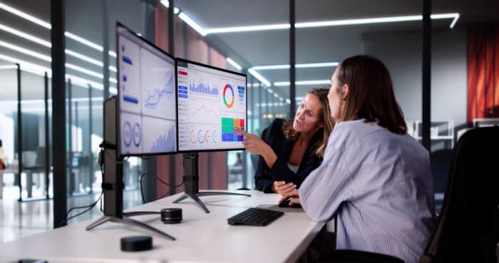 Two colleagues analyzing data on dual monitors.