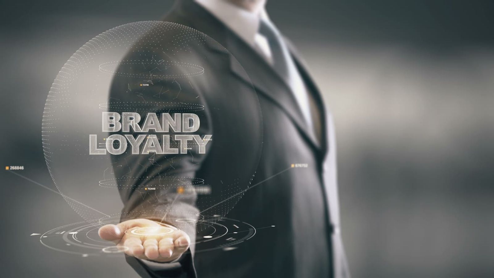 A person in a suit extends their hand, with a holographic projection above it displaying the words "BRAND LOYALTY" surrounded by futuristic digital graphics and circular patterns, seamlessly blending business with advanced technology.