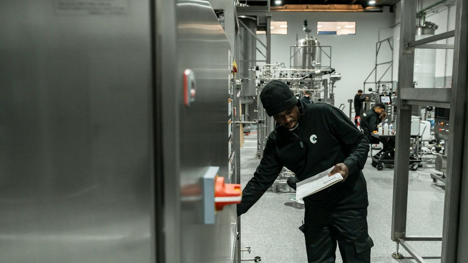A technician inspecting industrial equipment in a manufacturing facility while holding a checklist.