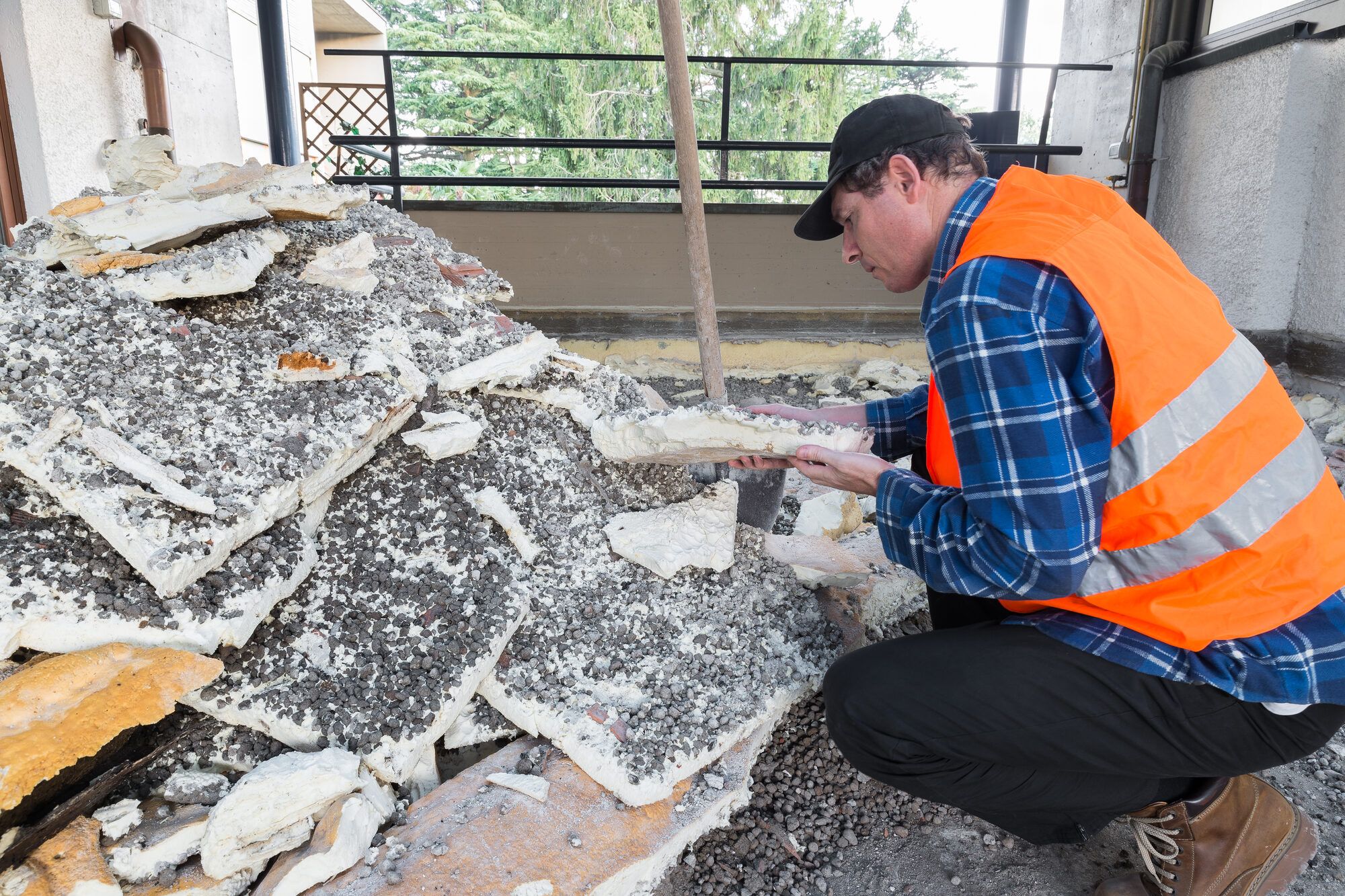 An inspector in a hi-vis vest examining suspected asbestos-containing debris at a job site