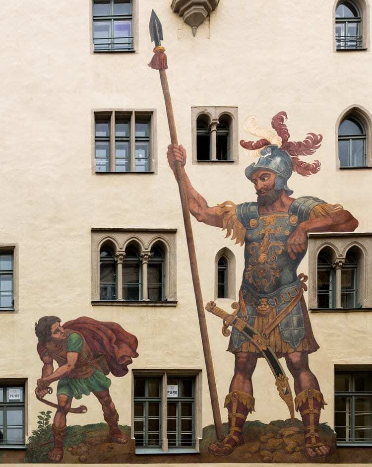 A mural on a building in Madison, WI, depicts the biblical scene of David and Goliath. On the left, David, a young shepherd, holds a sling poised to throw a stone. On the right, Goliath, a giant armored warrior holding a spear. The mural serves as an emblem for our marketing agency embracing asymmetric marketing strategies.