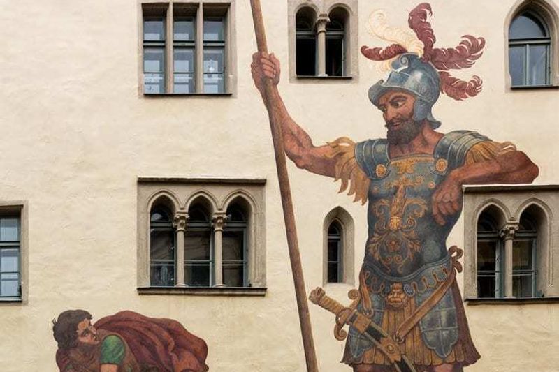 A mural on a building in Madison, WI, depicts the biblical scene of David and Goliath. On the left, David, a young shepherd, holds a sling poised to throw a stone. On the right, Goliath, a giant armored warrior holding a spear. The mural serves as an emblem for our marketing agency embracing asymmetric marketing strategies.