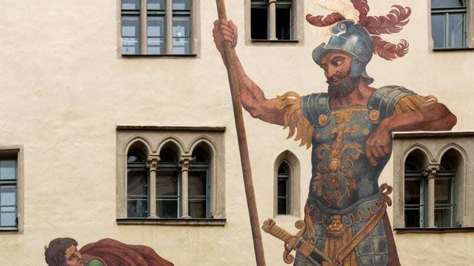 A mural on a building in Madison, WI, depicts the biblical scene of David and Goliath. On the left, David, a young shepherd, holds a sling poised to throw a stone. On the right, Goliath, a giant armored warrior holding a spear. The mural serves as an emblem for our marketing agency embracing asymmetric marketing strategies.