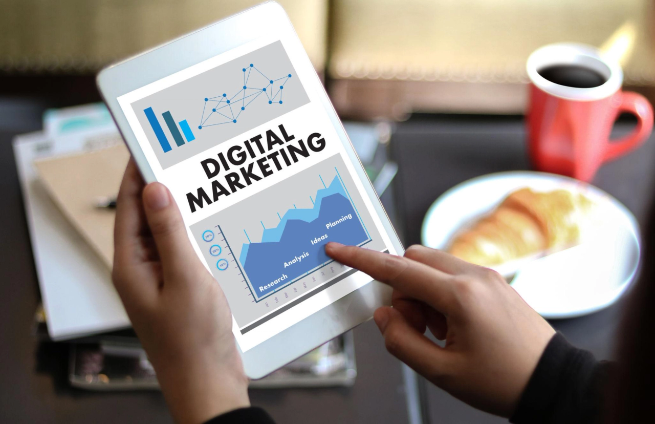 Hands holding a tablet showing a digital marketing dashboard, with a rising chart segmented into research, analysis, ideas and planning.