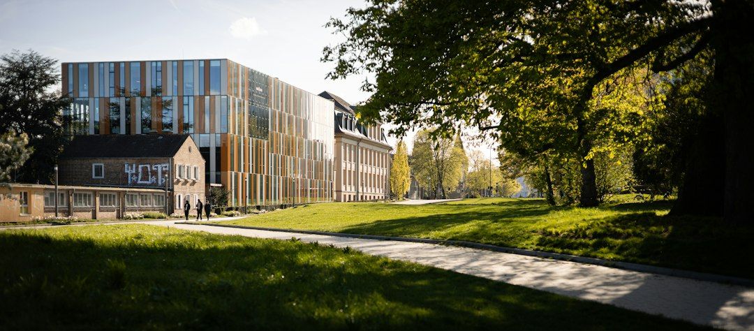 A modern university building beside an older campus building, surrounded by a green park.