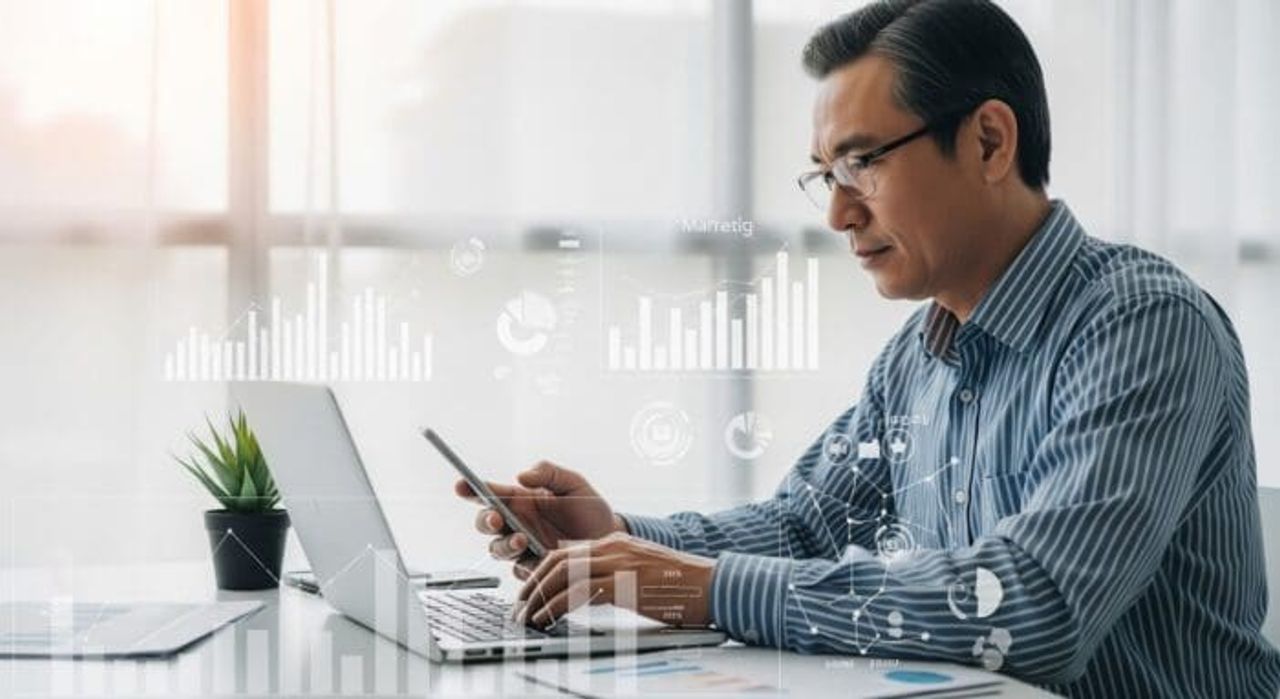 Man analyzing data on laptop and smartphone.