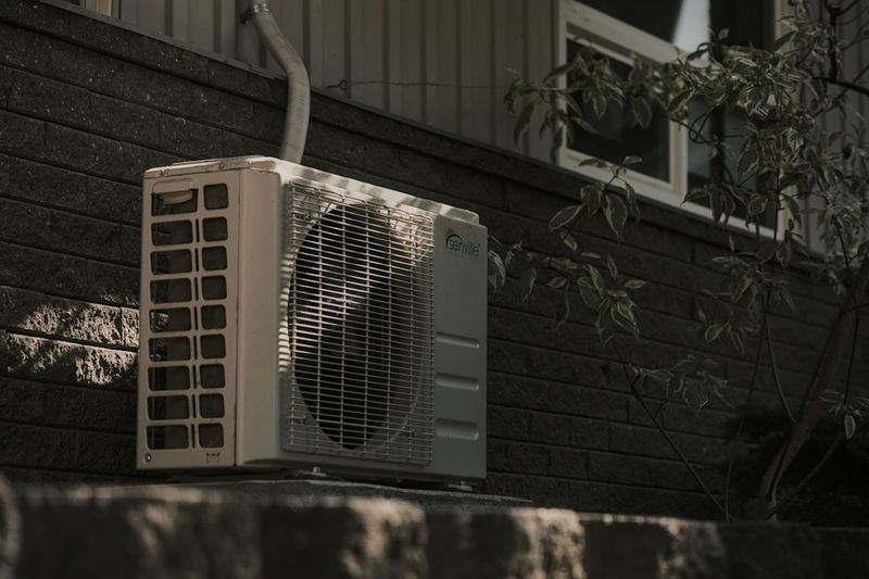 An outdoor air conditioning condenser unit against the brick wall of a house.