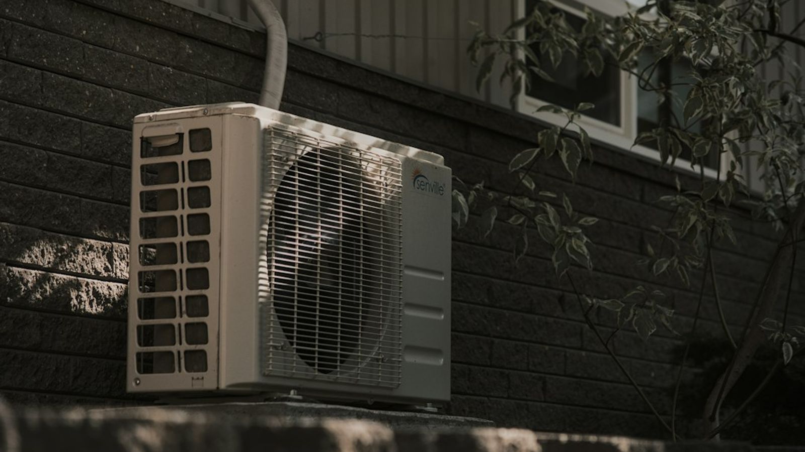 An outdoor air conditioning condenser unit against the brick wall of a house.