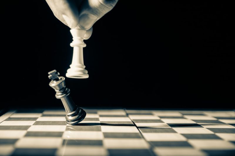 A white chess king toppling a black king — finding the one weakness you can attack