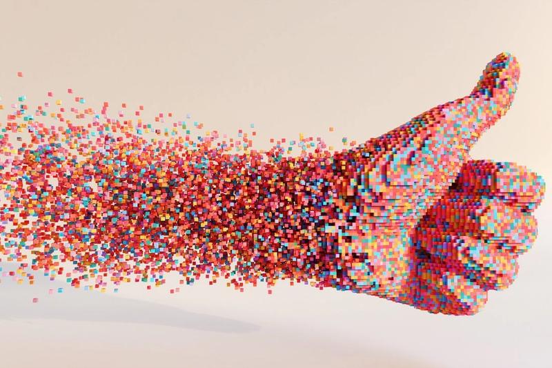 A thumbs-up hand gesture composed of numerous small, colorful cubes disintegrates into the air, creating a dynamic, pixelated effect against a light beige background—a modern take on digital marketing in Madison, Wisconsin.