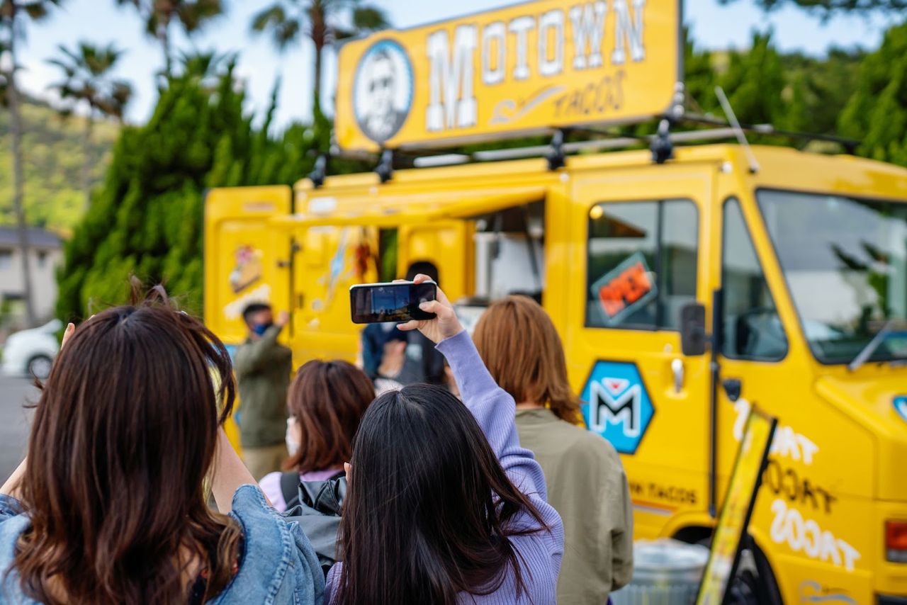 Crowd takes photos of yellow food truck.