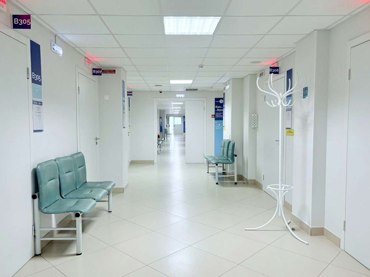 An empty hospital corridor with benches and doors along both sides.