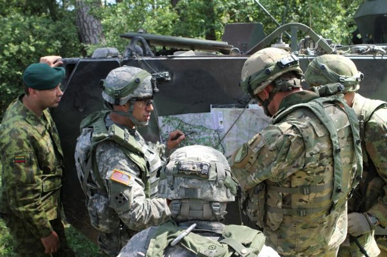 A group of military personnel in camouflage uniforms and helmets gather around a map on the side of an armored vehicle in a forest setting. Applying the art of war in your business, one soldier points to a location on the map as others closely observe and discuss their strategy.