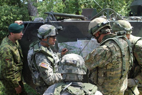 A group of military personnel in camouflage uniforms and helmets gather around a map on the side of an armored vehicle in a forest setting. Applying the art of war in your business, one soldier points to a location on the map as others closely observe and discuss their strategy.