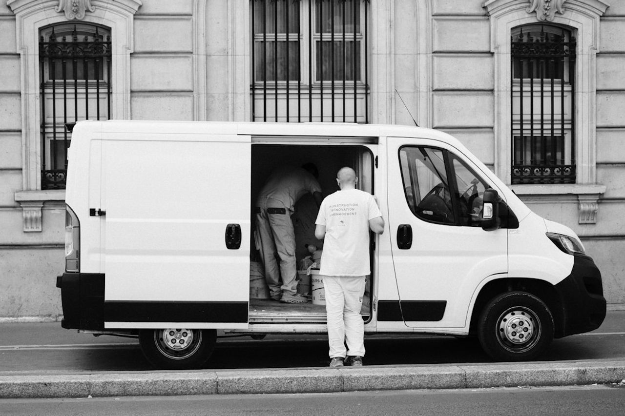 A tradesperson unloading supplies from the side door of a white work van.