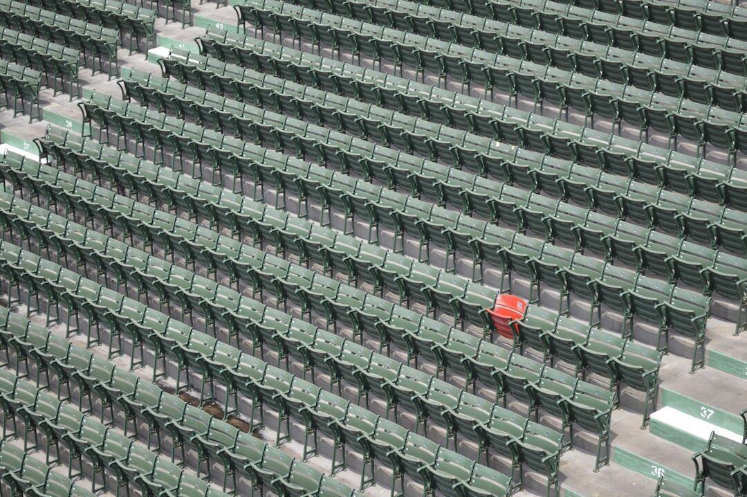 Rows of identical green stadium seats with one red seat among them, standing apart from every other seat in the block.