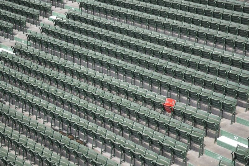 Rows of identical green stadium seats with one red seat among them, standing apart from every other seat in the block.
