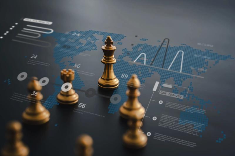 A chessboard with golden chess pieces is placed on top of a digital world map with data visualizations, charts, and graphs. The king piece is the focus in the center, symbolizing strategic decision-making and global analytics—a true business wargame unfolding before your eyes.