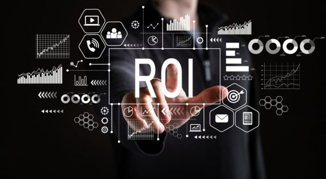 A hand is pointing towards the letters "ROI" displayed on a transparent screen filled with various business-related icons and graphs, representing concepts such as analytics, data, growth, and investment. The background is dark, highlighting the illuminated elements related to the marketing budget.