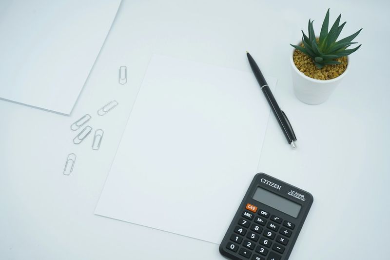 A calculator, a pen, and a blank sheet of paper on a desk.