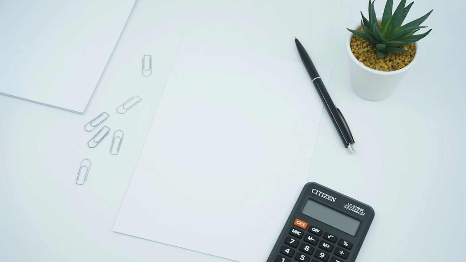 A calculator, a pen, and a blank sheet of paper on a desk.