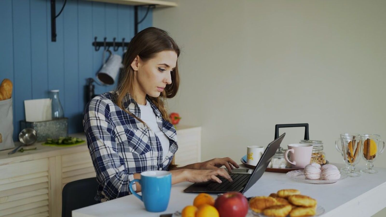 A business owner working through paperwork and figures on a laptop at a kitchen counter.