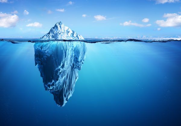 A massive iceberg floats in a blue ocean under a clear sky. About one-ninth of the iceberg is visible above the water, while the vast submerged part is seen beneath the surface, showcasing dark blue and icy textures below the waterline. Truly, luck favors the prepared who navigate these treacherous waters.