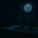 Dimly lit office with two monitors and a clock