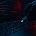 A gloved hand holding a USB drive near a laptop