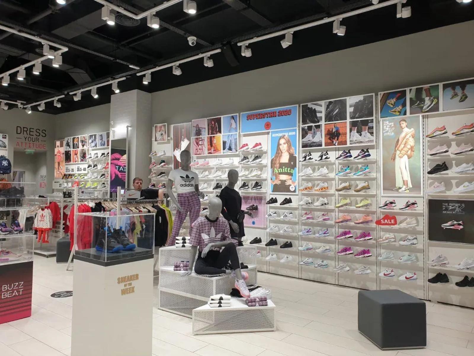Interior of a brightly lit modern sportswear store with walls of sneakers, mannequins, and promotional posters.