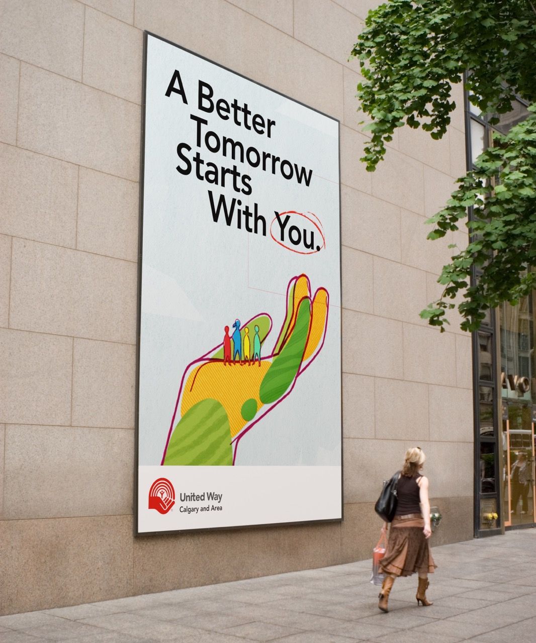 A billboard on a wall with the text "A Better Tomorrow Starts With You" and below the text is a large, colorful, illustrated hand with people standing in the palm.