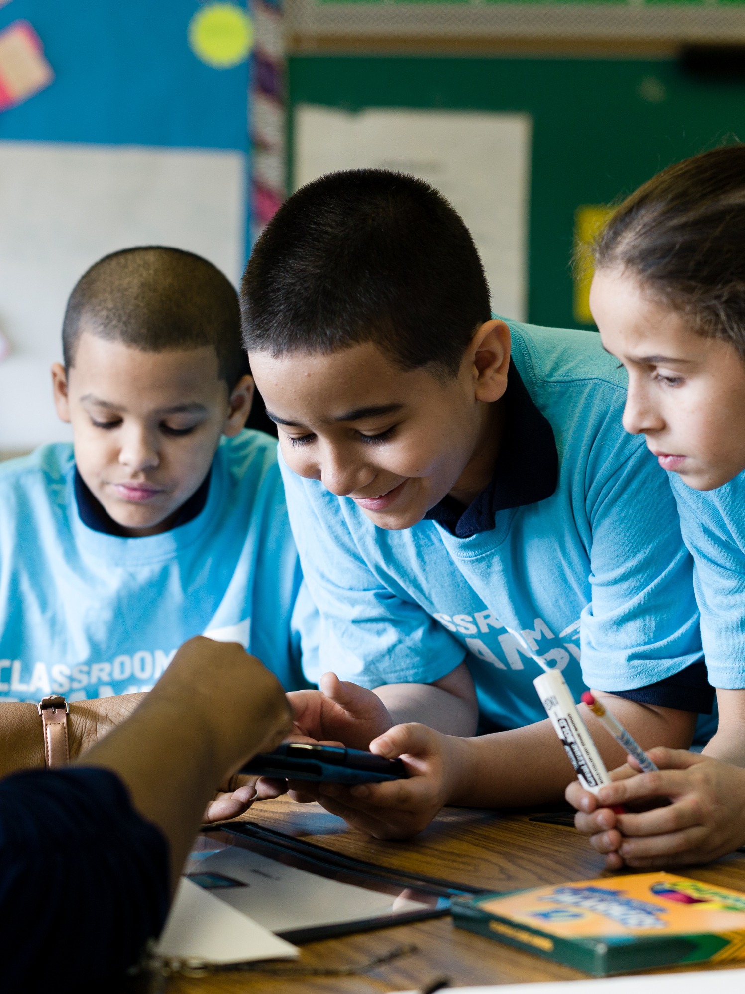 Kids in a classroom learning while wearing t-shirts with Classroom Champions' logos on them.