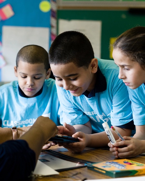 Kids in a classroom learning while wearing t-shirts with Classroom Champions' logos on them.