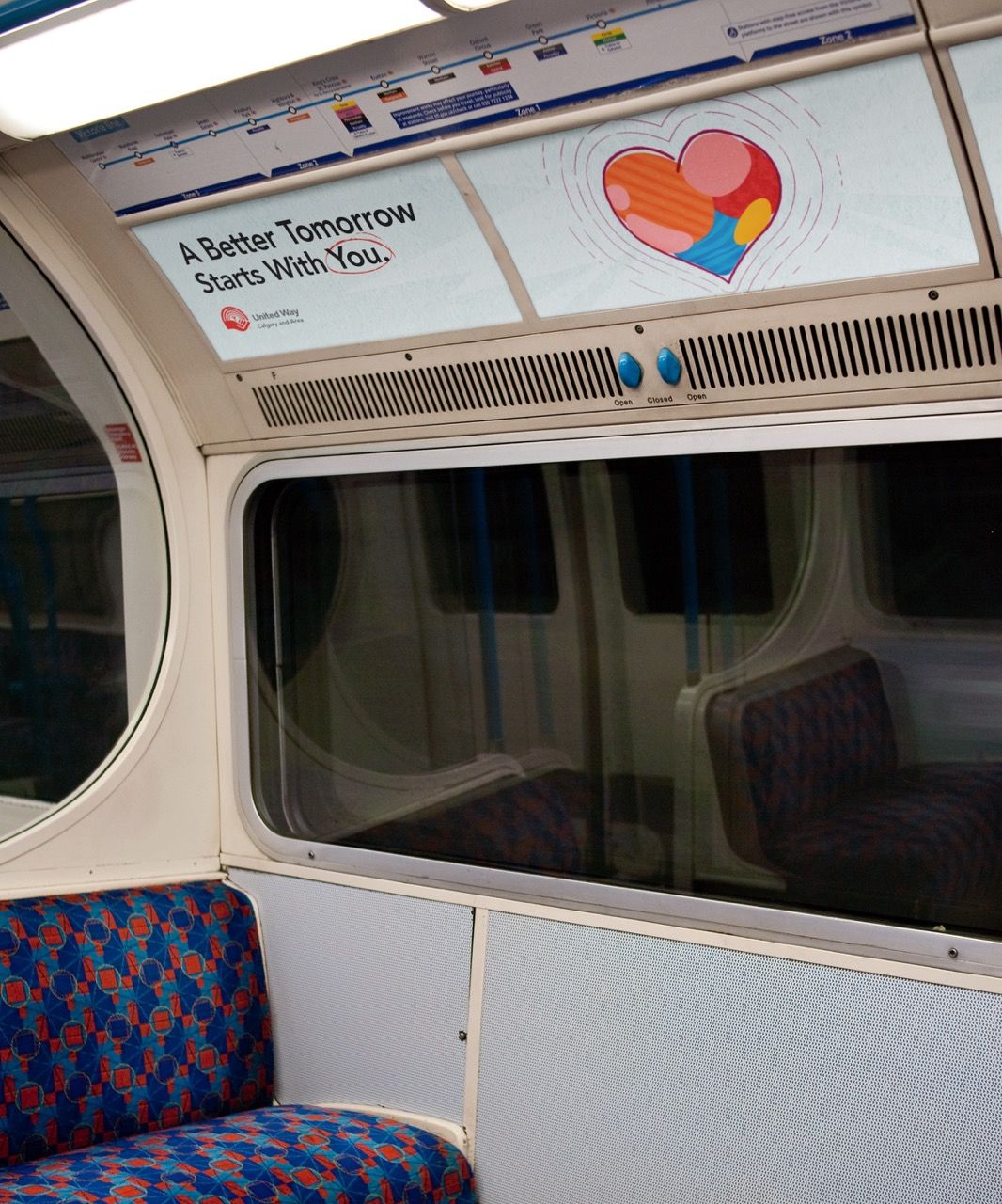 The inside of a train car looking at a seating bench with an advertisement with a heart and text saying "A Better Tomorrow Starts With You" above.