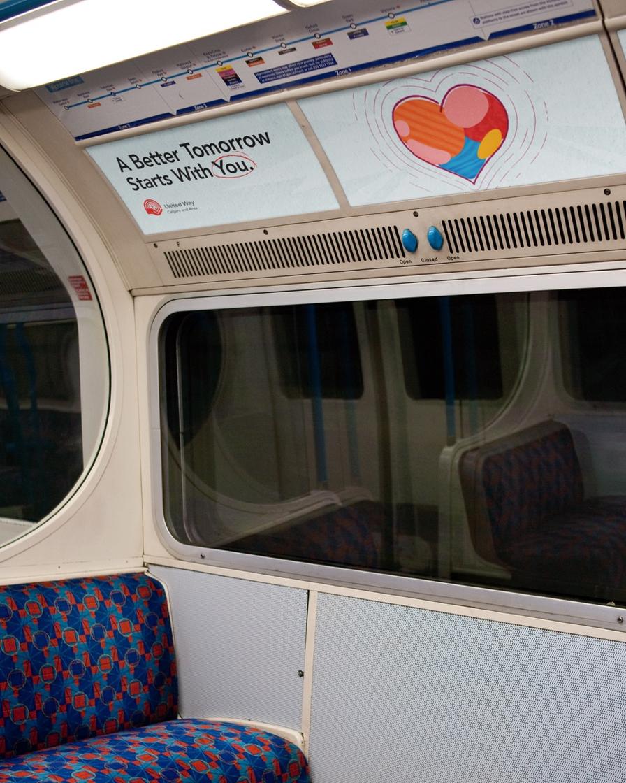 The inside of a train car looking at a seating bench with an advertisement with a heart and text saying "A Better Tomorrow Starts With You" above.