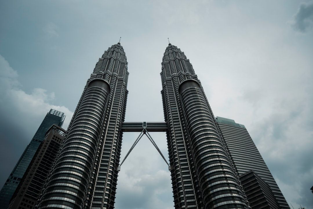 Twin skyscrapers connected by a skybridge under cloudy sky