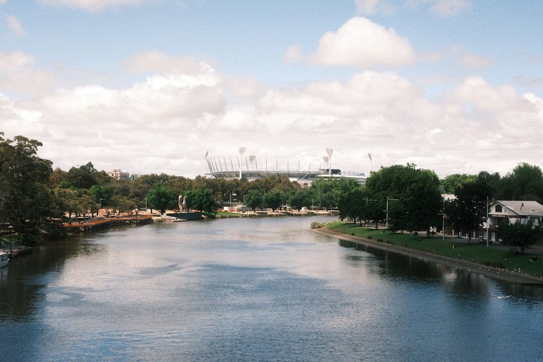 River with stadium and trees under cloudy sky