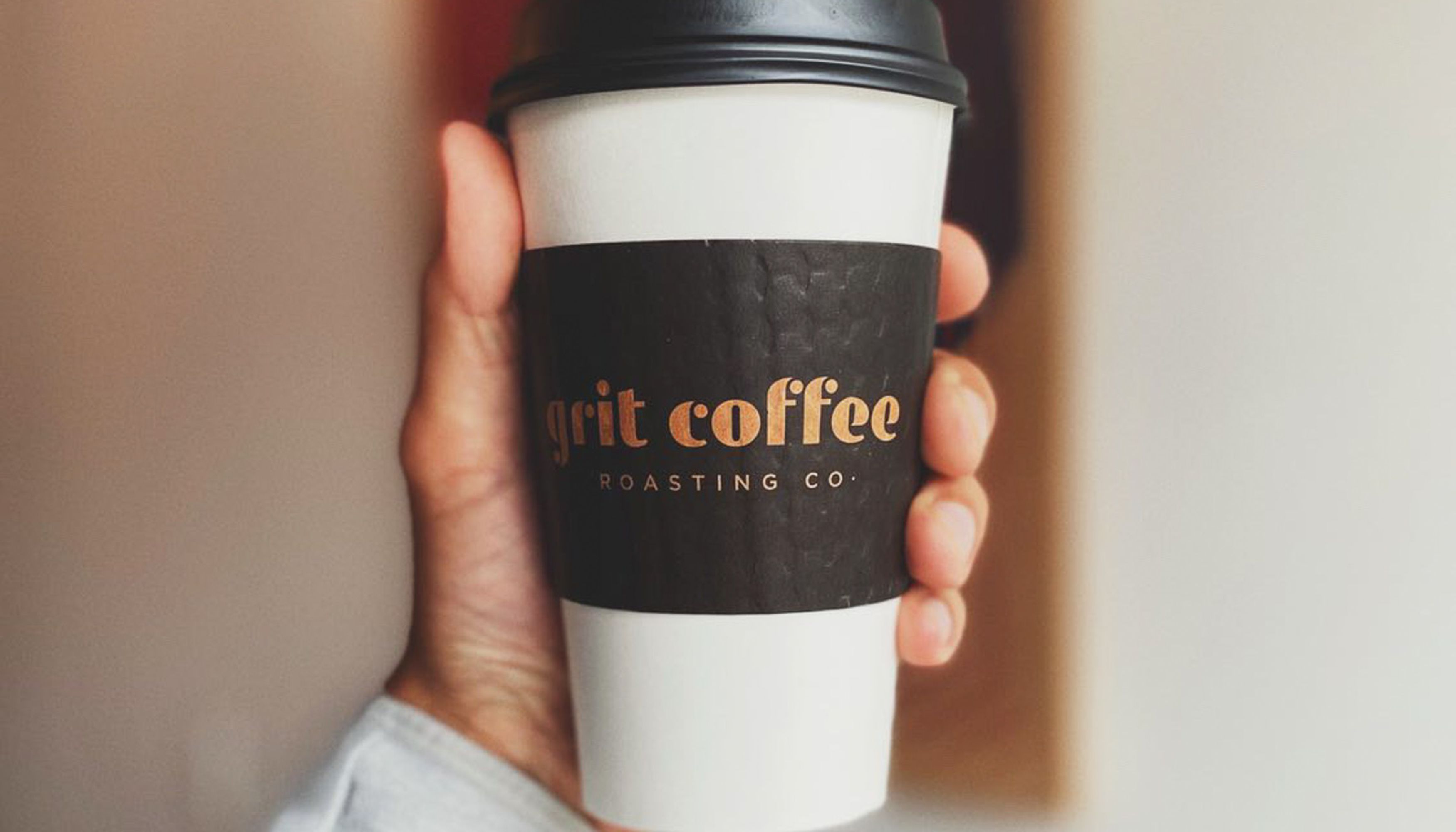 Hand holding a hot cup of Grit coffee