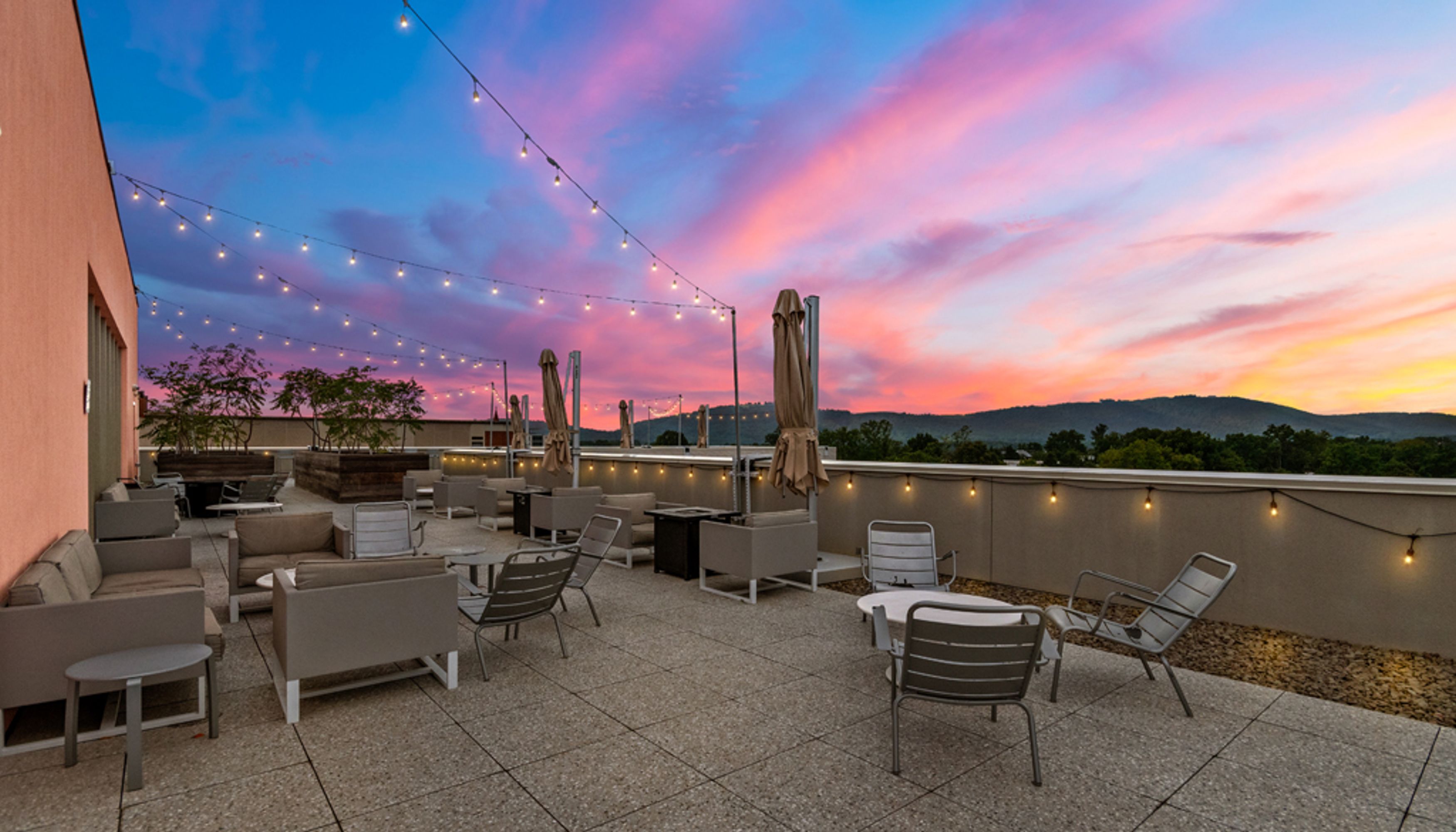 tables and chairs on a rooftop with string lights and sunset viewundefined