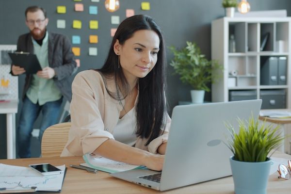 Woman working on laptop with man behind her