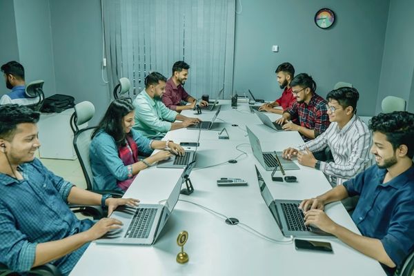 a group of people sitting around a table with laptops