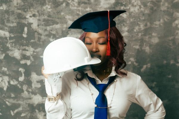 A graduate holds a hard hat with a graduation cap.