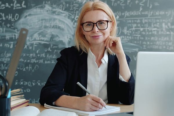 A female teacher smiling at the desk with a laptop.